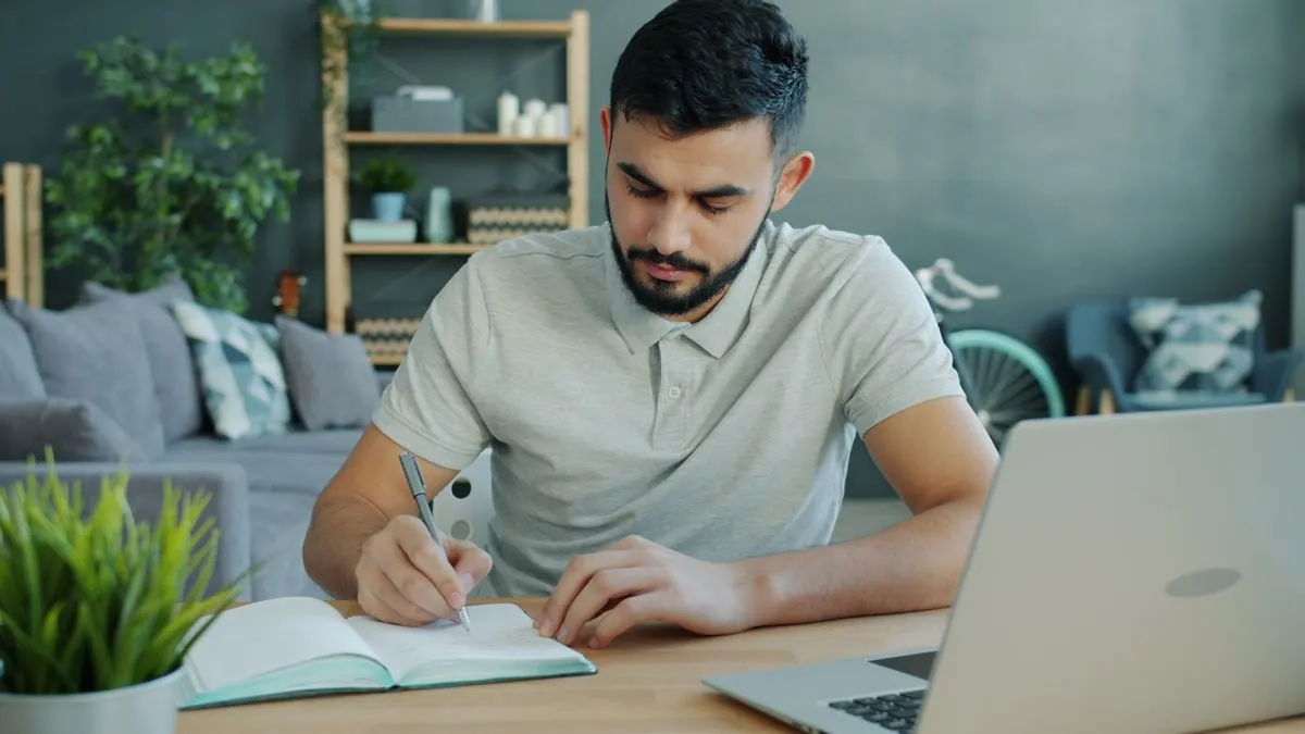 Muž si dělá poznámky u notebooku doma