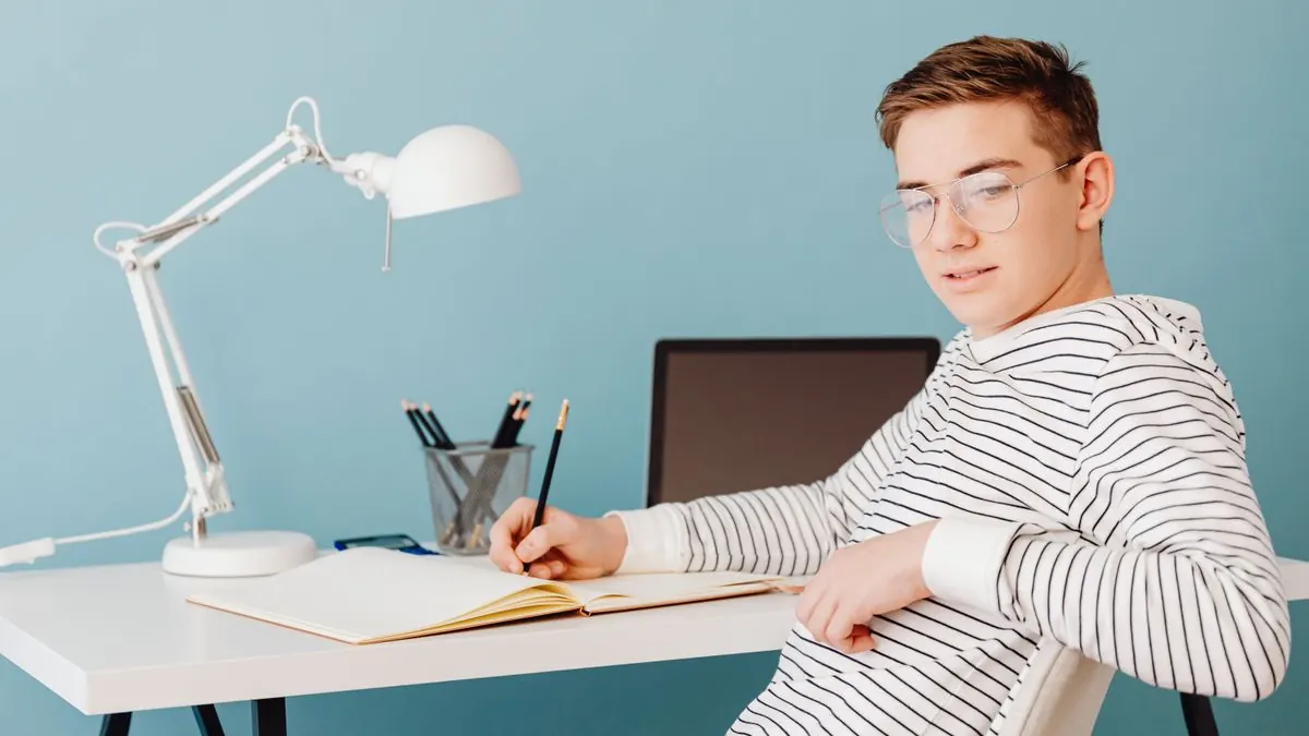 Student v brýlích studuje u stolu s lampou