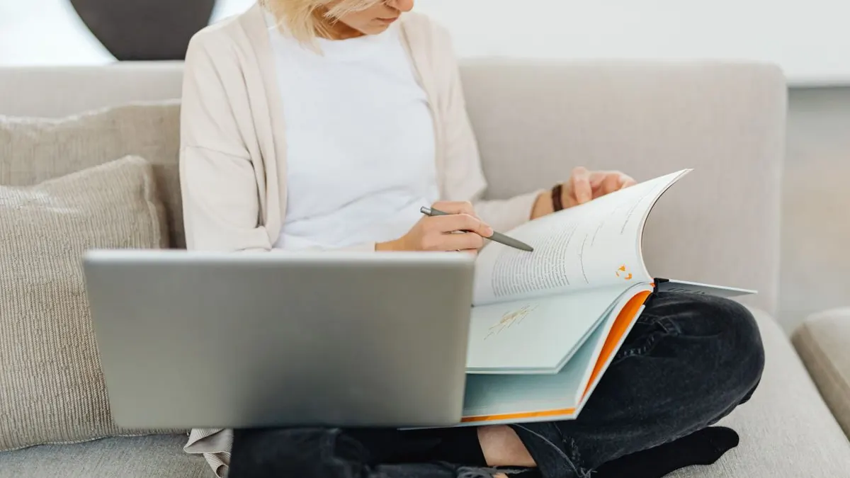 Žena na gauči studuje s notebookem a knihou