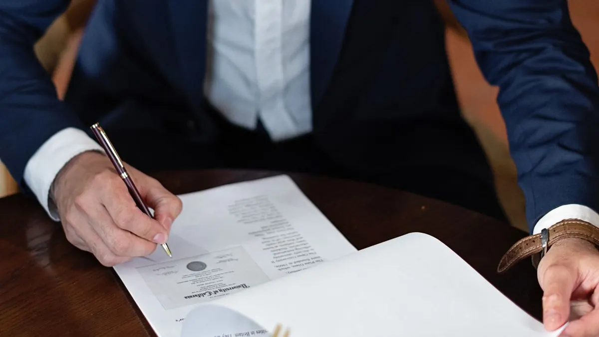 Muž v saku podepisuje dokument vedle kolegy