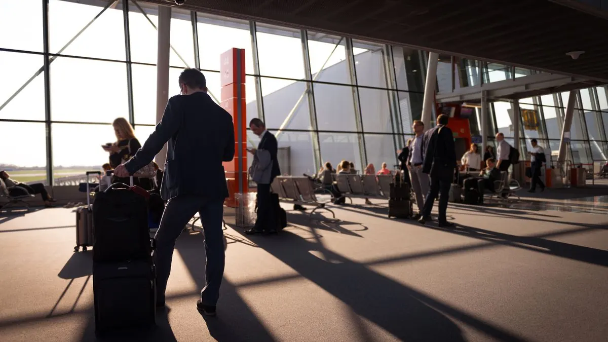 Muž kráčí s kufrem prosluněným letištním terminálem