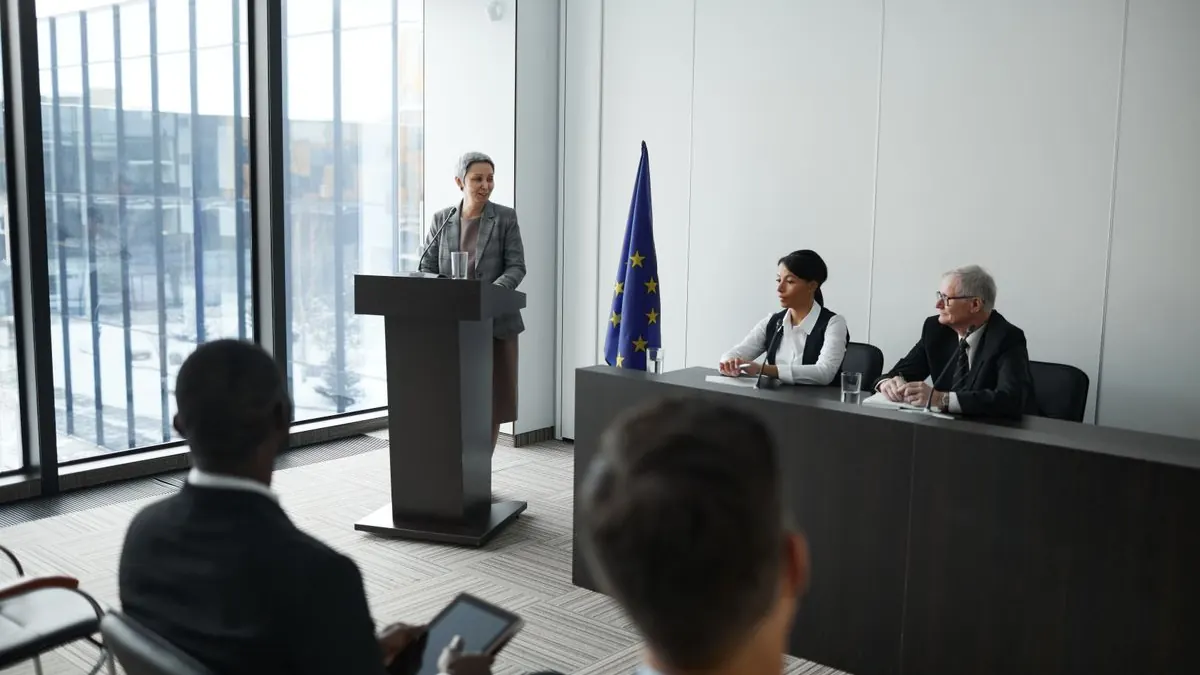 Žena mluví z pódia před vlajkou EU