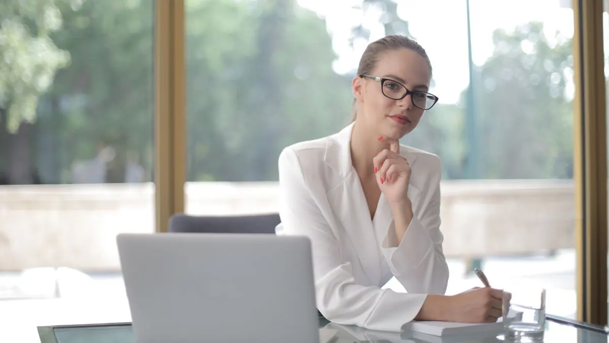 Žena zamyšleně sedí u notebooku u okna