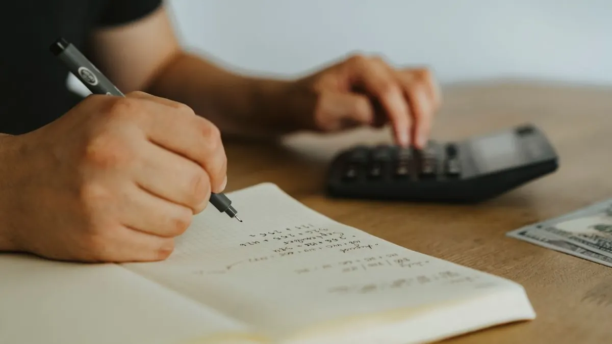 Ruka píše výpočty do notesu u kalkulačky