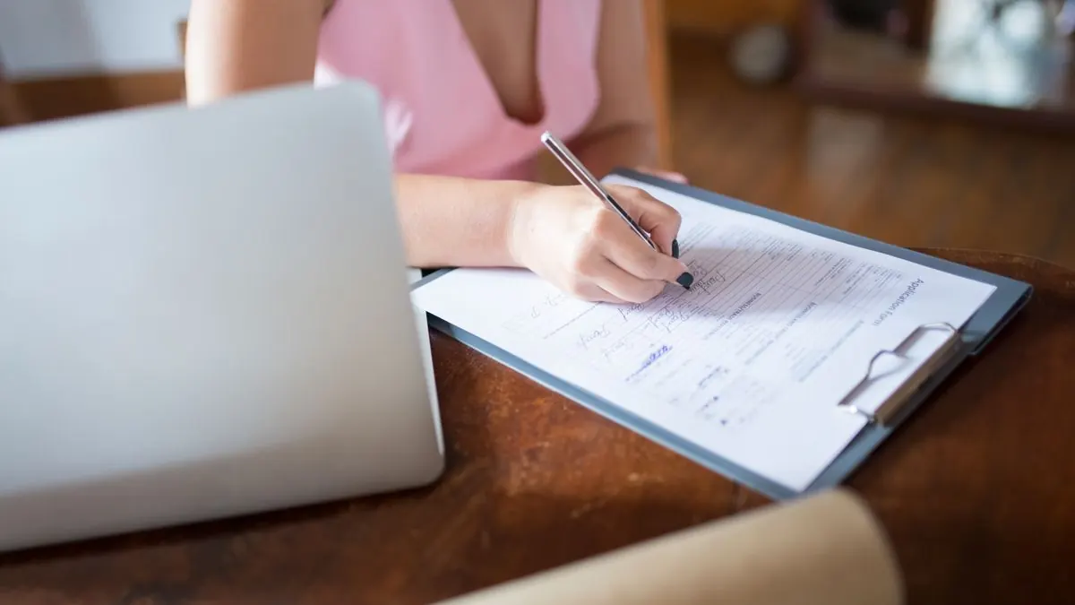 Žena vyplňuje formulář na desce vedle notebooku