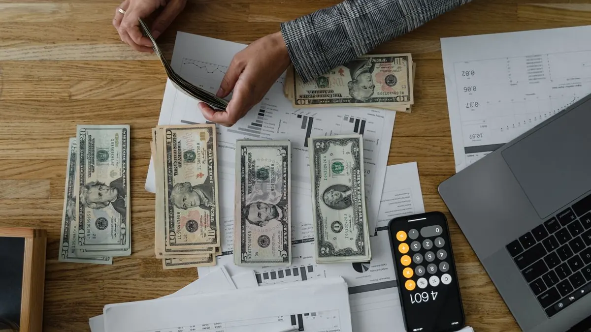 Ruce s dolarovými bankovkami vedle notebooku na stole