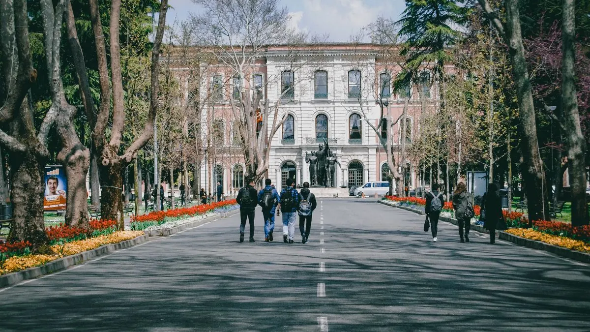 Studenti kráčejí širokou alejí mezi budovami univerzity