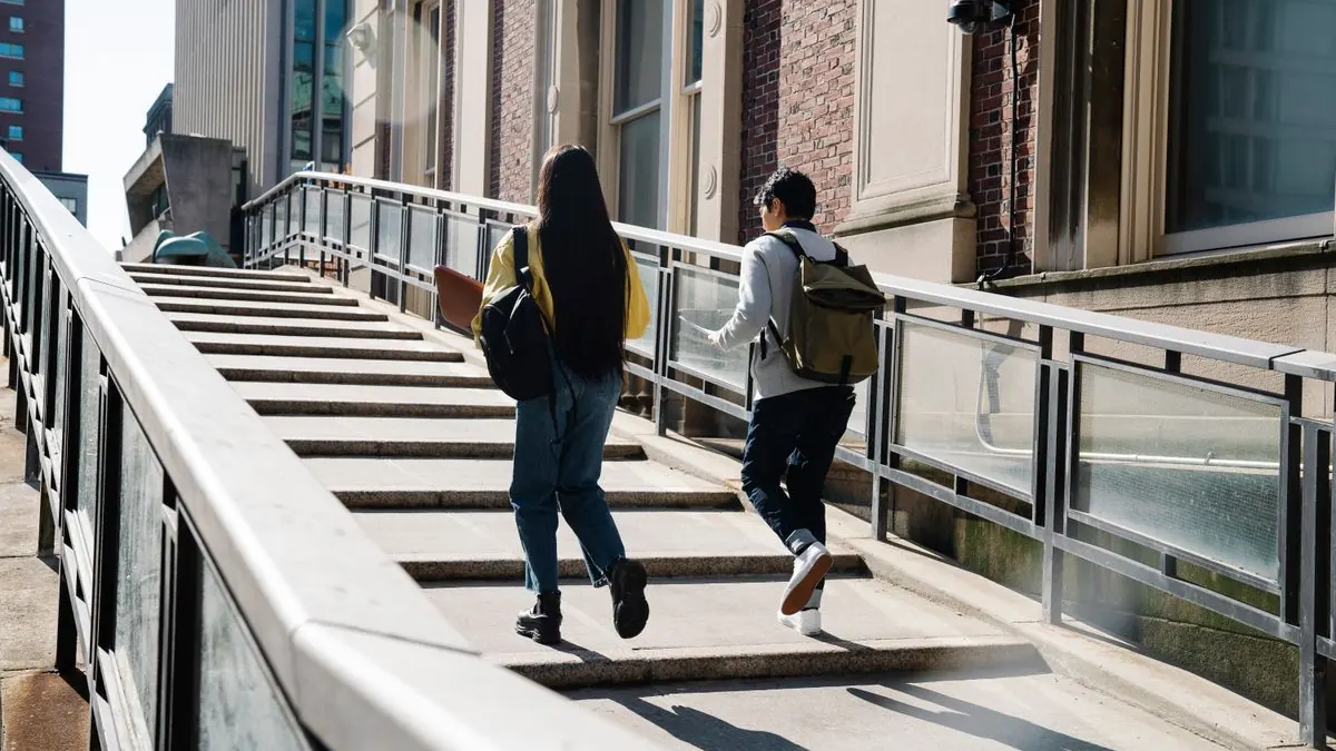 Studentka s batohem běží po rampě k budově