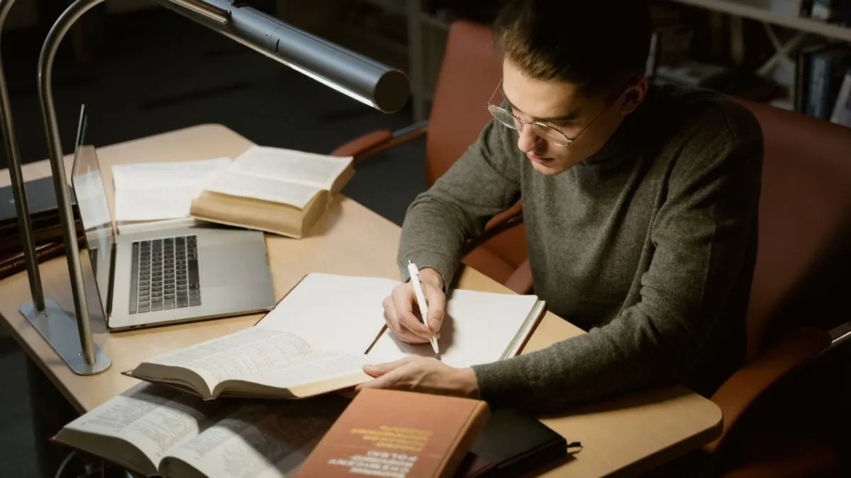 Muž píše poznámky u knih a notebooku v knihovně