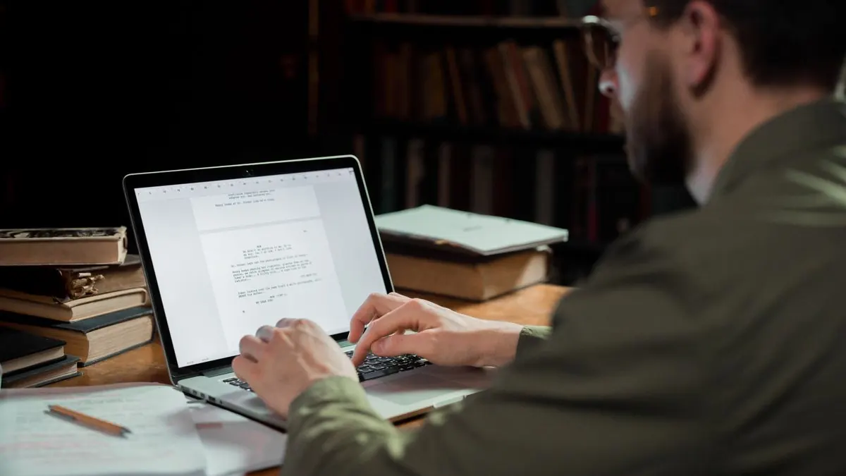Muž píše text na laptopu obklopený knihami