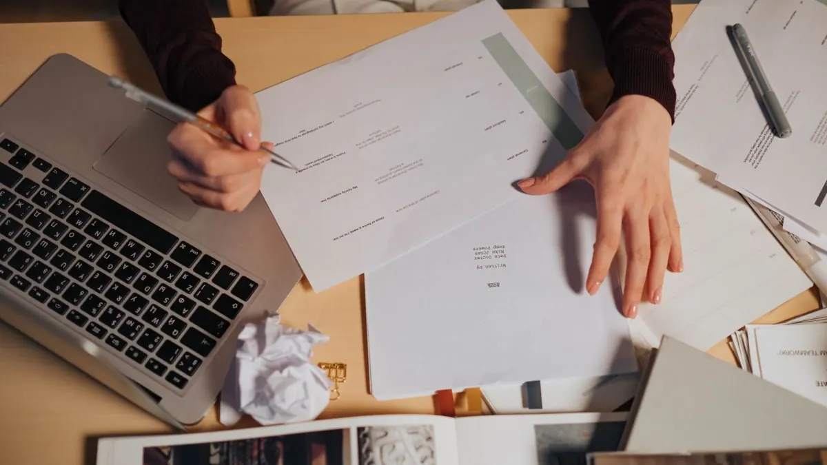 Ruce upravují rozházené podklady a text na laptopu